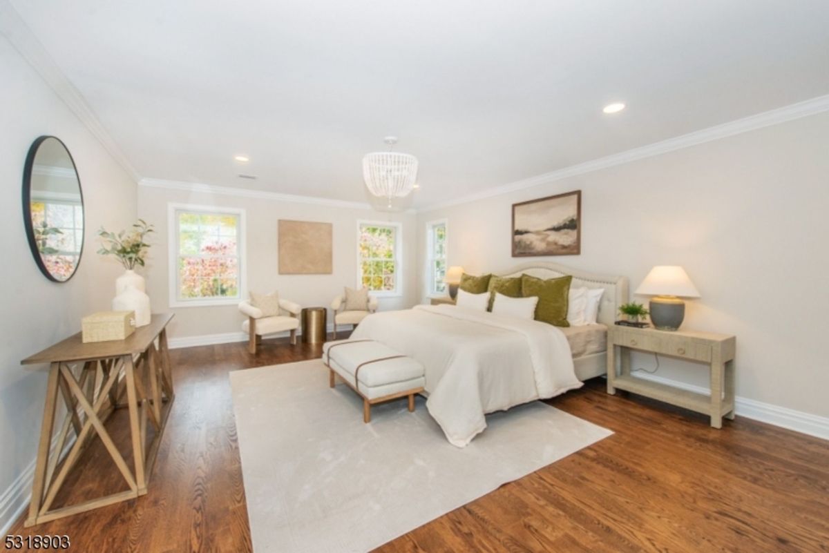 Primary bedroom features warm hardwood floors, soft neutral tones, and elegant furnishings with natural light streaming through multiple windows.