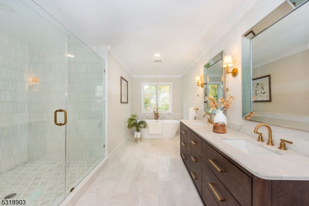 Elegant bathroom features a luxurious walk-in shower, a soaking tub by the window, and a dual-sink vanity with brass accents.