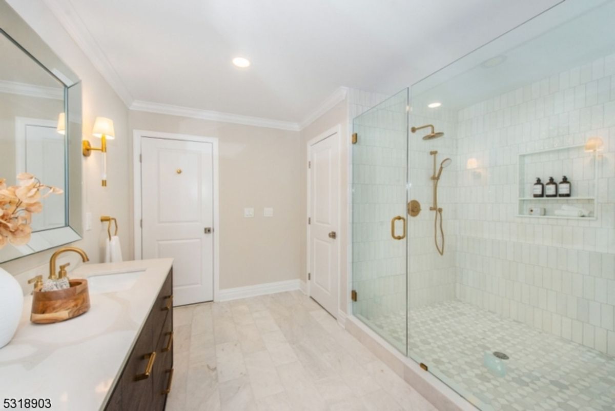 Bathroom showcases a glass-enclosed shower with brass fixtures and a sleek vanity with gold hardware.