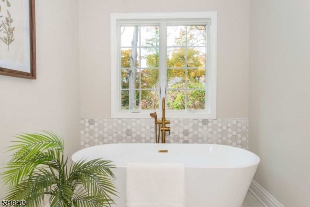 Freestanding soaking tub is set against a hexagonal tile backdrop beneath a large picture window.