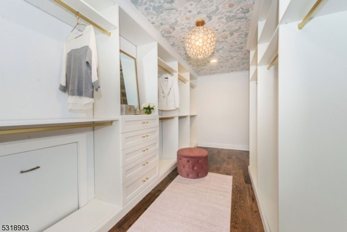 Custom walk-in closet features built-in shelving, gold accents, and a floral wallpapered ceiling with a decorative light fixture.