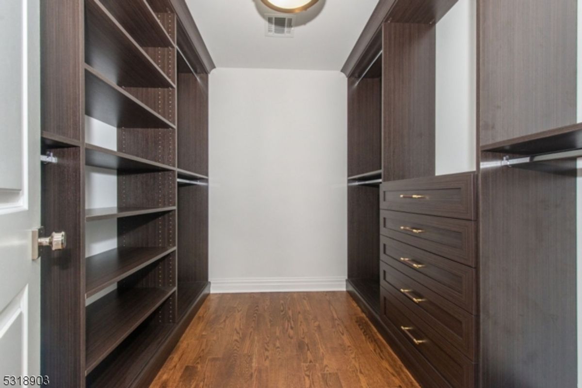 A sleek, modern walk-in closet showcases dark wood cabinetry with open shelving, gold hardware, and rich hardwood flooring.