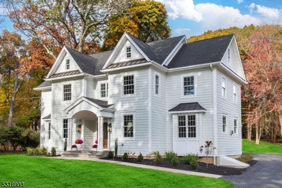 Stunning corner view highlights symmetrical architecture, black metal roof accents, and vibrant autumn foliage in the background.