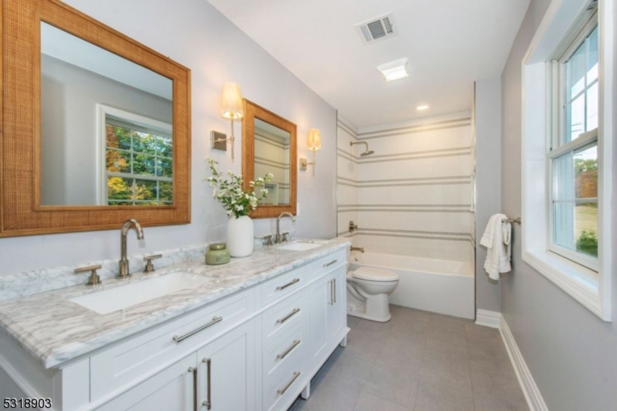 Spa-inspired bathroom offers a marble double vanity, elegant wall sconces, and a striped-tile tub for a modern yet cozy ambiance.