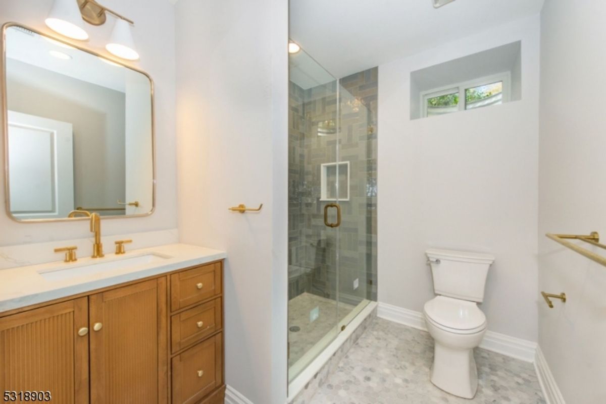 A stylish bathroom features brass fixtures, a glass-enclosed shower, and a warm wood vanity for a modern yet classic look.