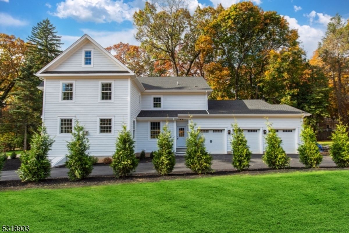 A crisp white exterior with a three-car garage is set against vibrant autumn foliage, blending elegance with functionality.