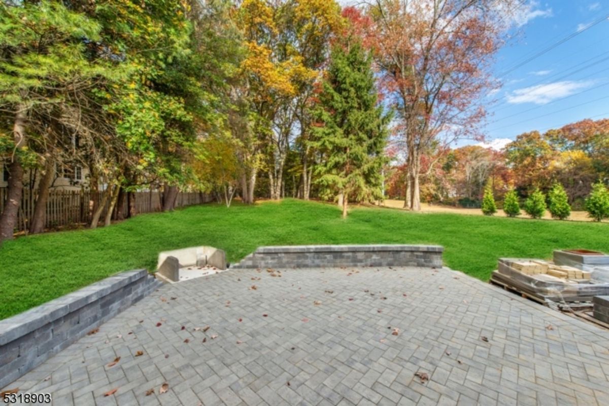 A paved patio leads to a lush, tree-lined backyard offering tranquility and privacy.