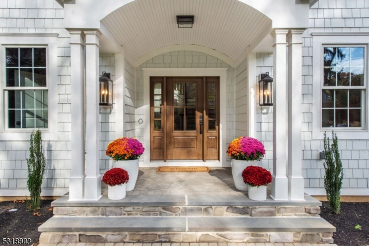 Entryway showcases a wooden double door framed by crisp white siding, columns, and vibrant potted flowers.