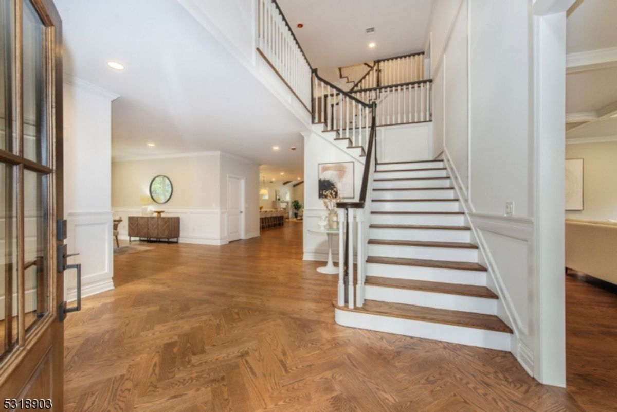 Grand foyer features a staircase with dark wood accents, elegant wainscoting, and herringbone-patterned hardwood floors.