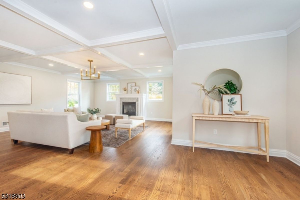 Living room showcases coffered ceilings, a modern chandelier, and a cozy fireplace framed by soft neutral tones.