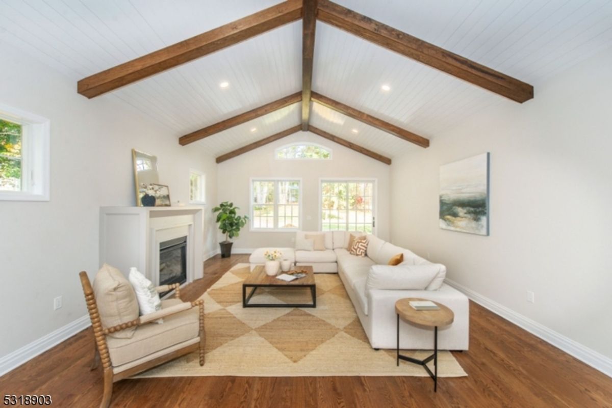 Vaulted ceiling with exposed wooden beams enhances the cozy yet spacious living area featuring a fireplace and abundant natural light.