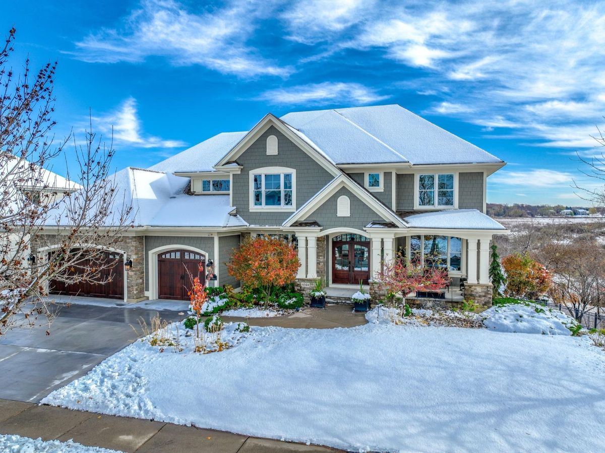 An elegant two-story home featuring a stone-accented facade, covered porch, and scenic snowy surroundings.