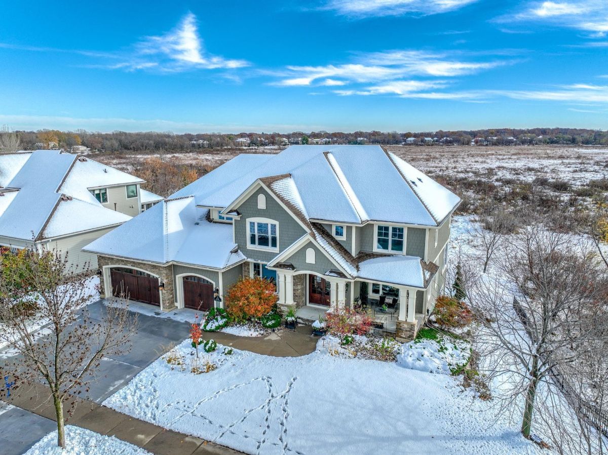 A charming snow-covered home with a three-car garage and picturesque views of the surrounding fields.