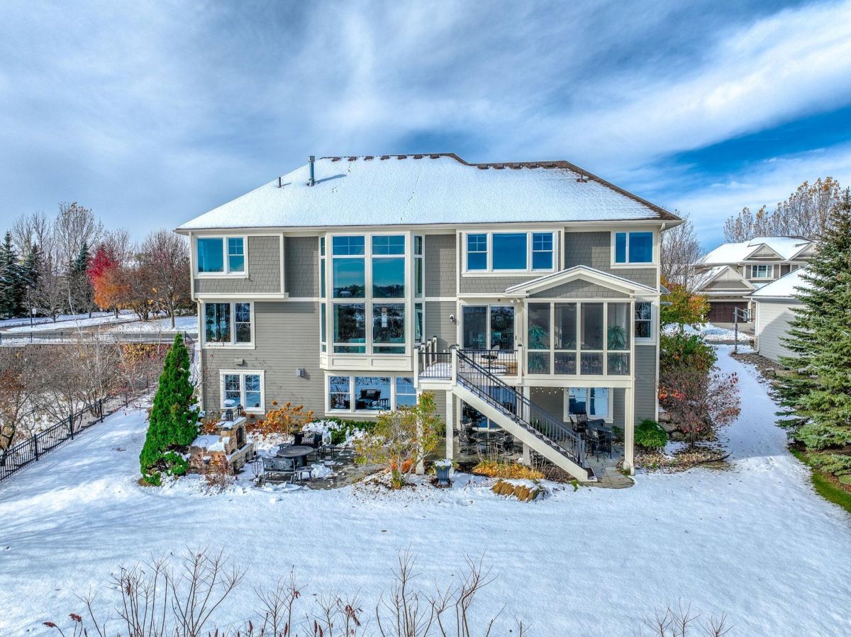 Snow-dusted backyard showcases a grand home with expansive windows and a tiered outdoor space.