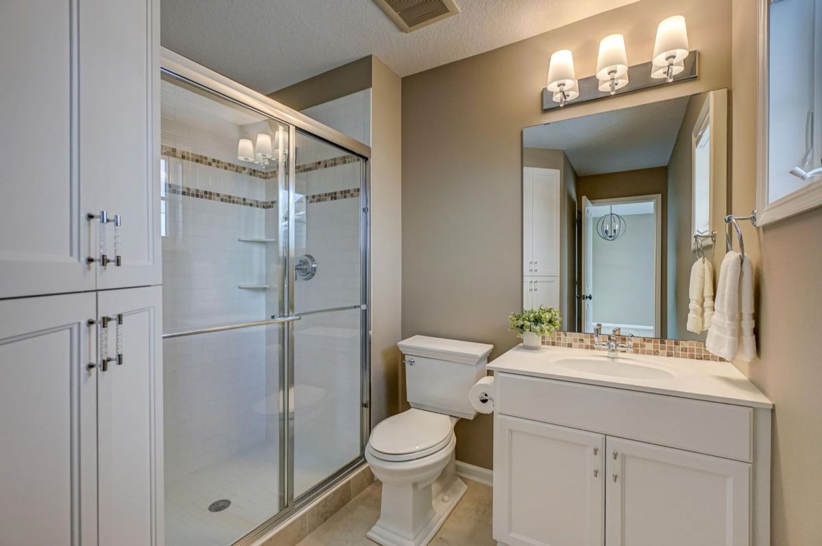 A well-lit bathroom featuring a glass-enclosed shower and ample storage cabinetry.