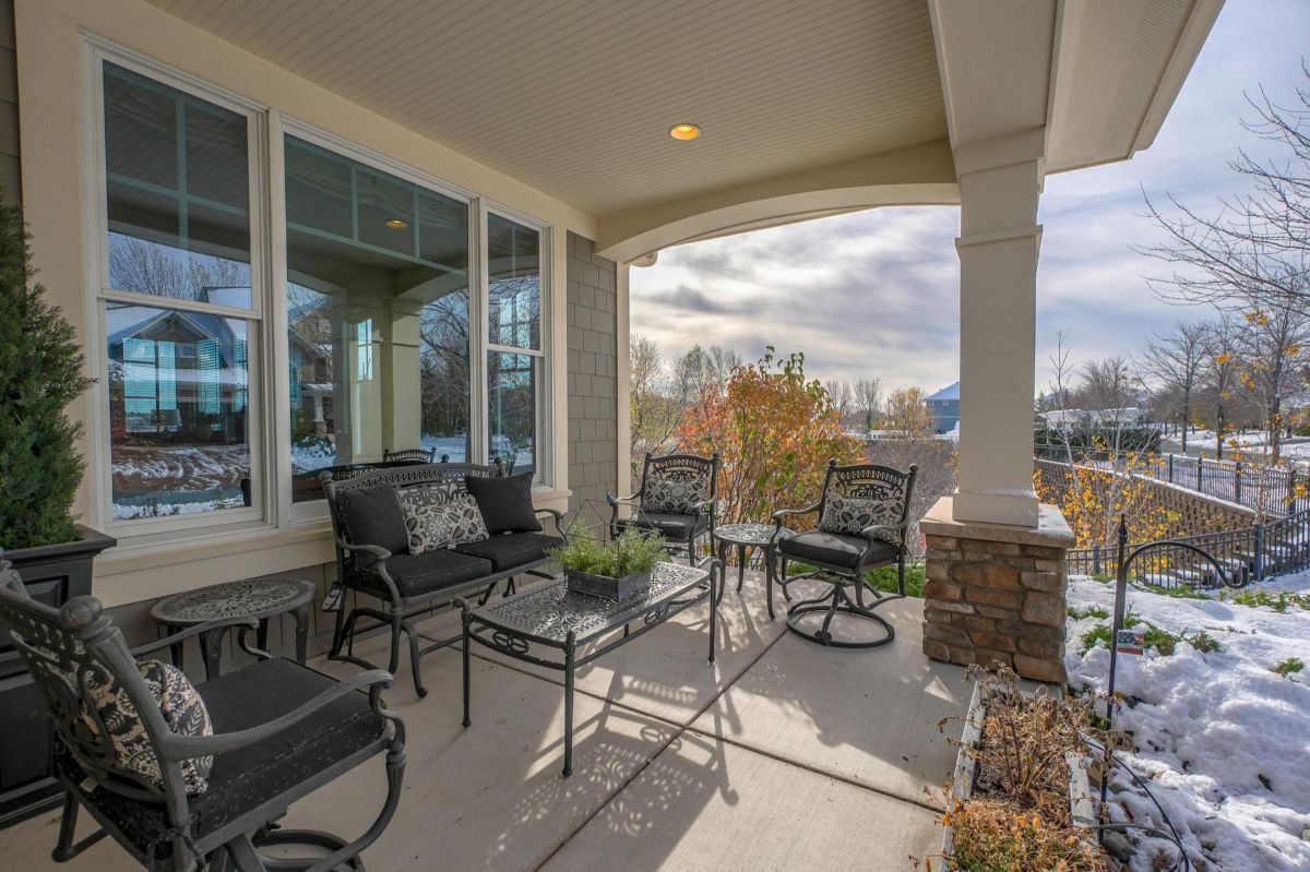 An inviting covered patio features elegant wrought iron seating with plush cushions, overlooking a serene winter landscape.