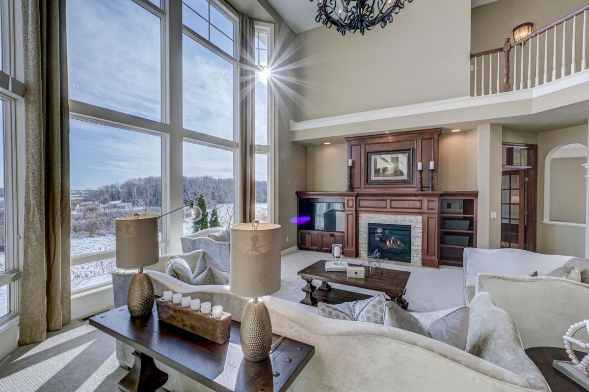 Living room features soaring floor-to-ceiling windows that frame picturesque views, complemented by a grand fireplace and elegant custom woodwork.