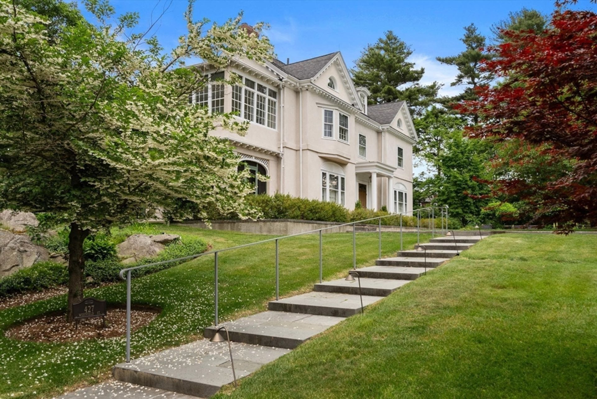 A charming residence stands gracefully atop a sloping lawn, surrounded by blossoming trees and well-manicured greenery.