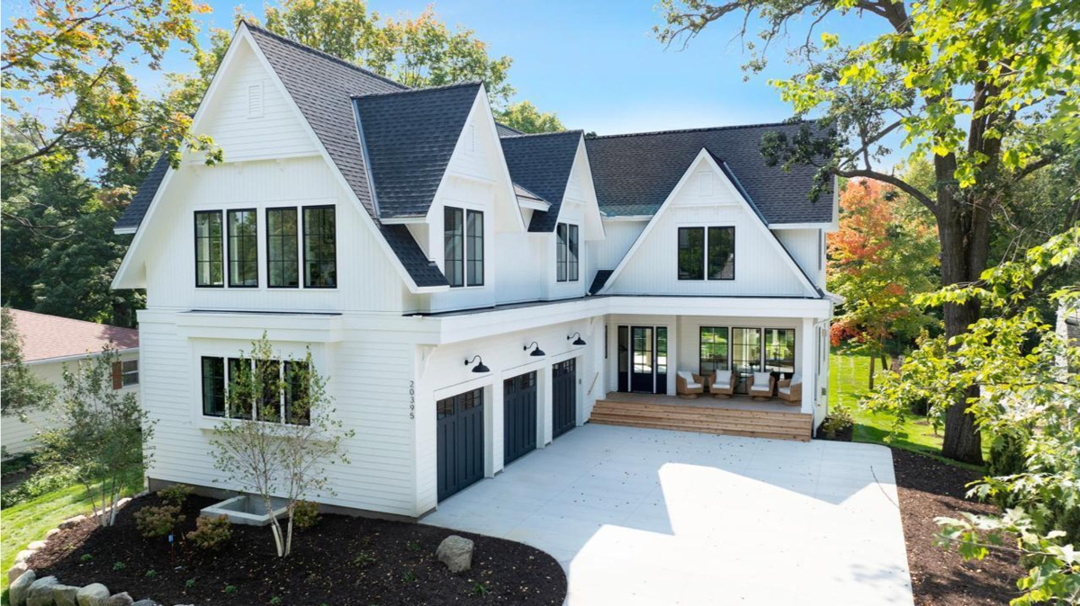 A stunning modern farmhouse with crisp white siding, black accents, and a spacious front porch surrounded by lush greenery.