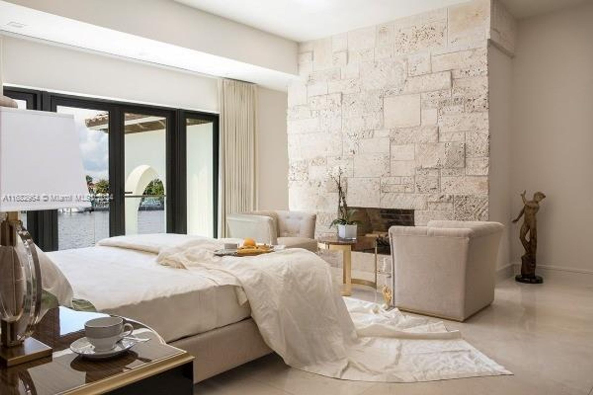 Bedroom combines soft textures with a stone accent wall and opens to a water-view terrace.