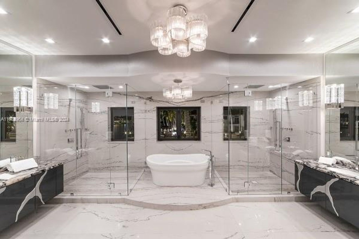 An opulent bathroom showcases a freestanding soaking tub, glass-enclosed showers, and sleek marble surfaces under a radiant chandelier.