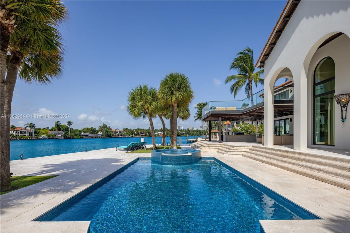 Expansive waterfront pool and patio area with lush palm trees and panoramic views of the serene blue canal.