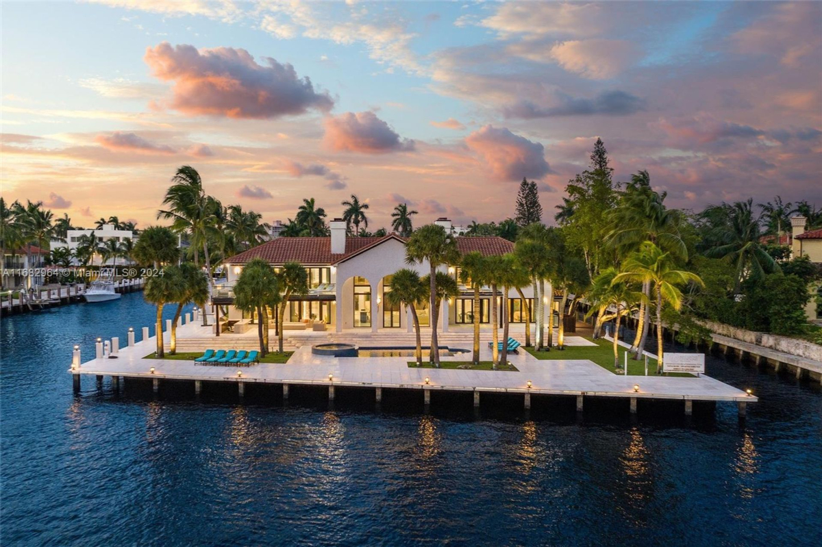 Waterfront estate glows under a breathtaking sunset, surrounded by swaying palms and serene waters.