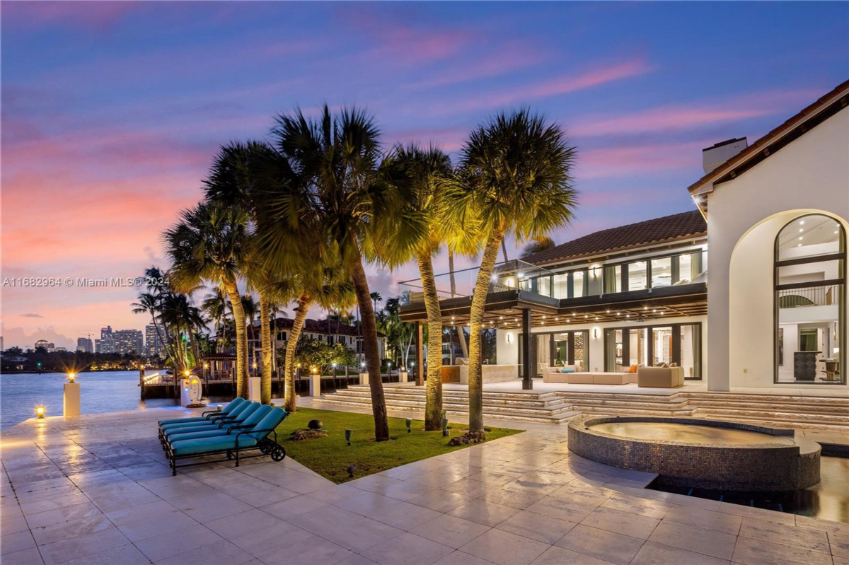 A waterfront luxury estate illuminated at sunset, highlighting its serene pool, elegant terrace, and lush palm surroundings.