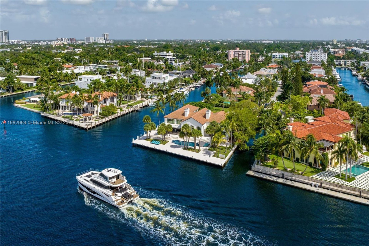 Idyllic waterfront neighborhood featuring luxurious estates with private docks, a yacht cruising through the serene canal, and lush greenery lining the waterways.