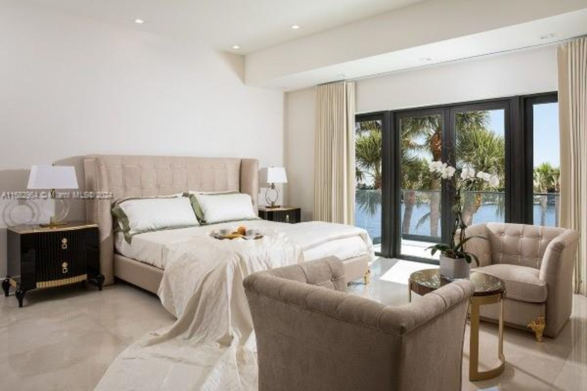 A sophisticated bedroom pairs plush seating with waterfront balcony views and natural light.