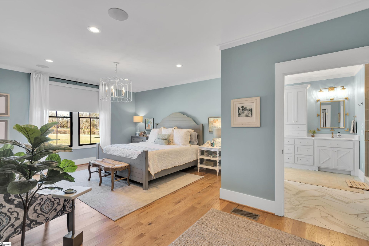 Serene bedroom suite featuring soft blue walls, elegant lighting, and a seamless transition to a luxurious ensuite bathroom.