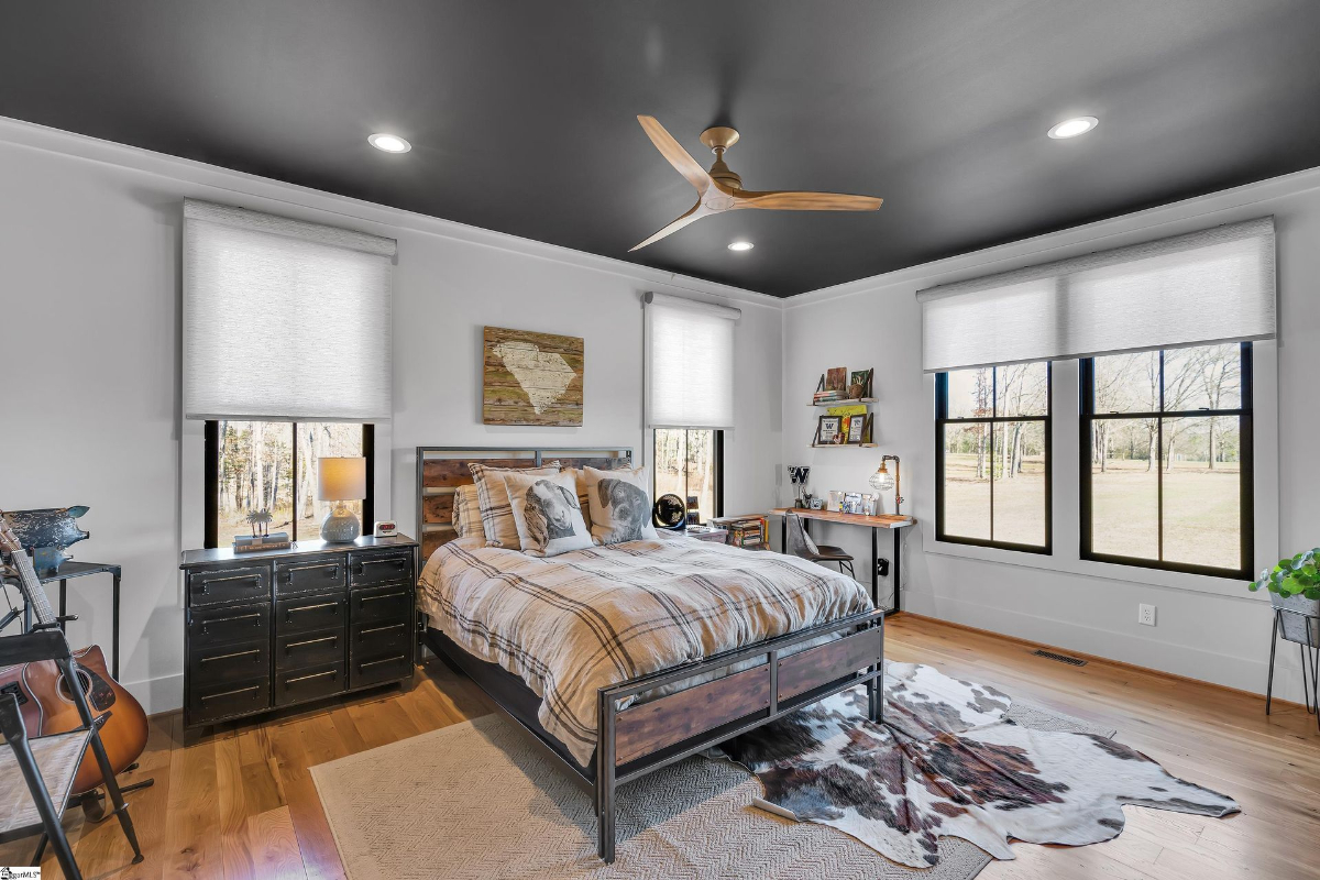 Bedroom with industrial accents, a bold black ceiling, and large windows overlooking the serene outdoors.