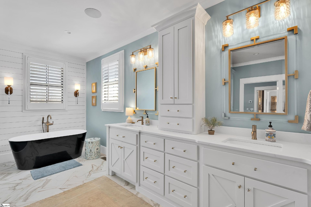 Luxurious bathroom featuring a freestanding black tub, double vanities, and gold accents against soft blue walls.