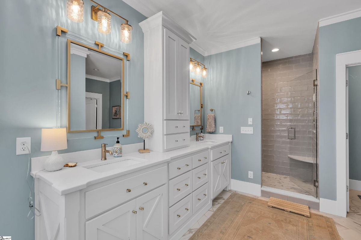 Sophisticated double vanity with sleek gold accents, a glass-enclosed shower, and calming blue walls.