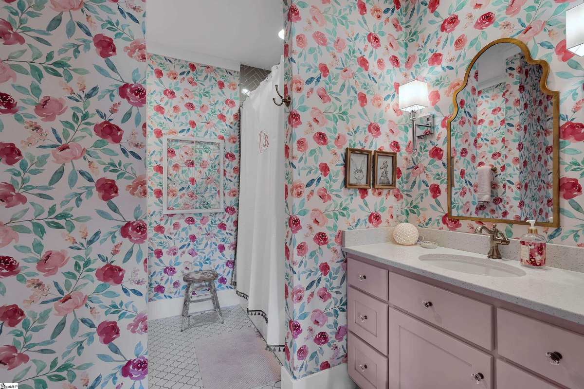 Whimsical bathroom adorned with vibrant floral wallpaper, a pastel pink vanity, and a scalloped mirror.