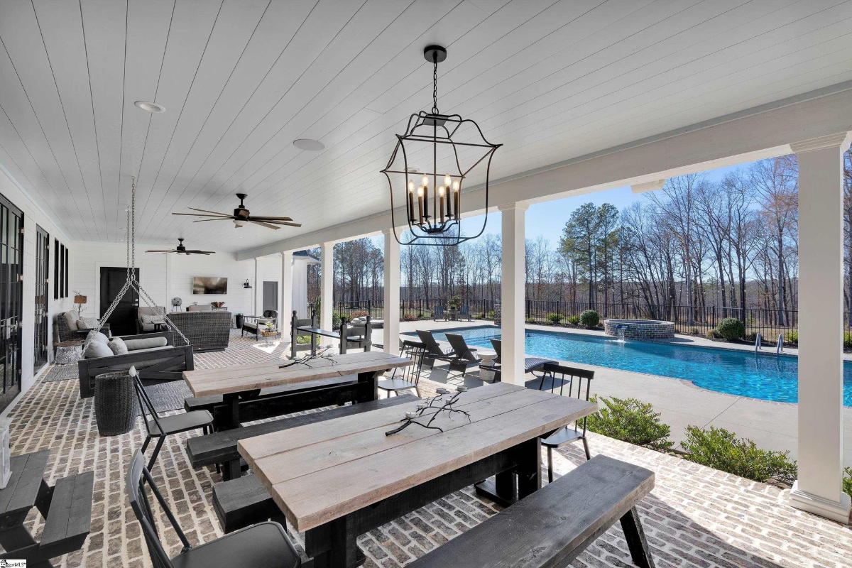 Expansive covered patio featuring rustic dining tables, cozy seating areas, and views of the sparkling pool and serene landscape.