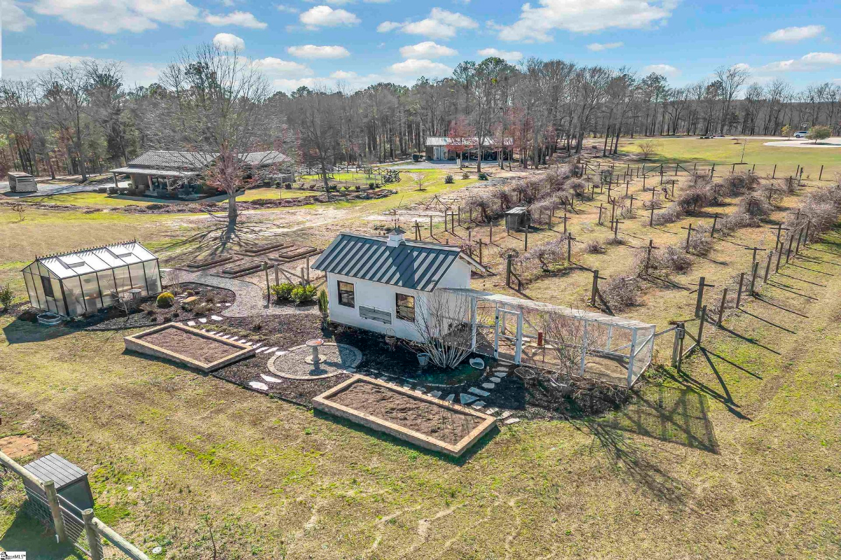 Charming garden area featuring raised beds, a greenhouse, and a chicken coop surrounded by sprawling vineyards.