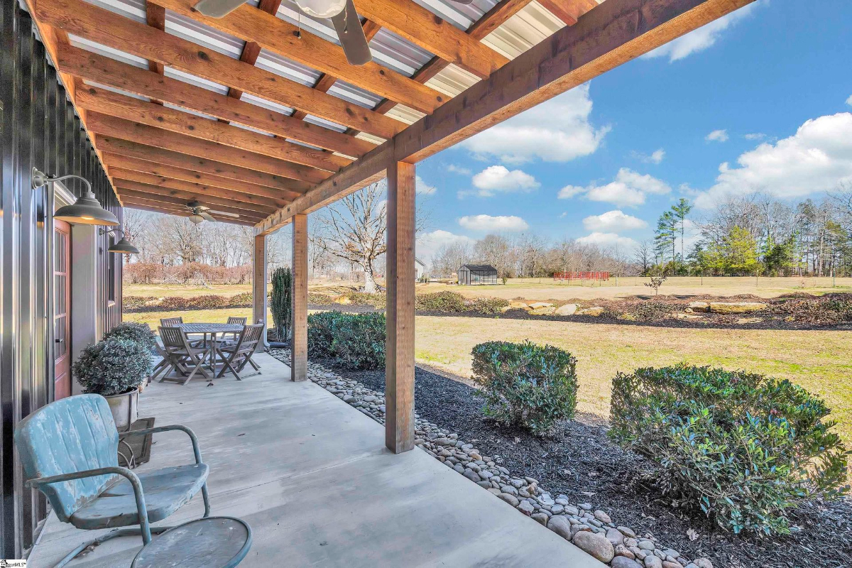 Covered porch with wooden beams, comfortable seating, and views of the expansive property.