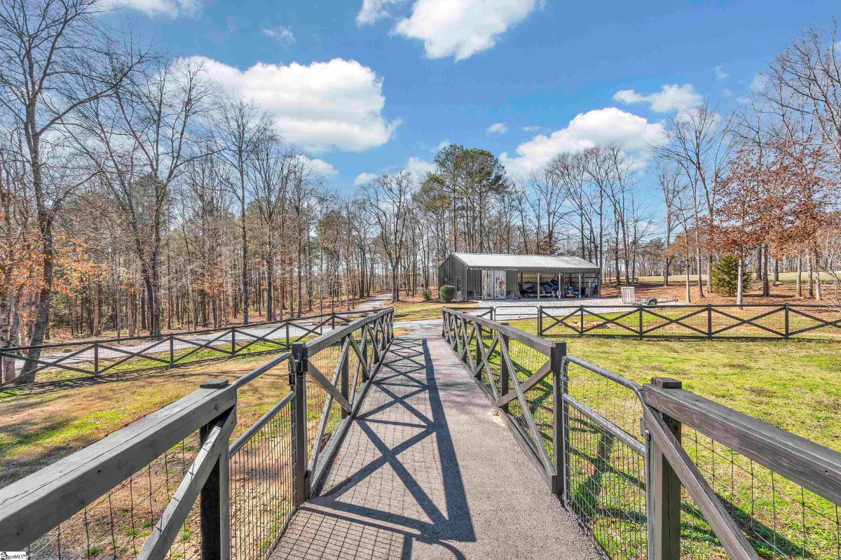 Expansive walkway leading to a charming outbuilding surrounded by fenced greenery and wooded views.