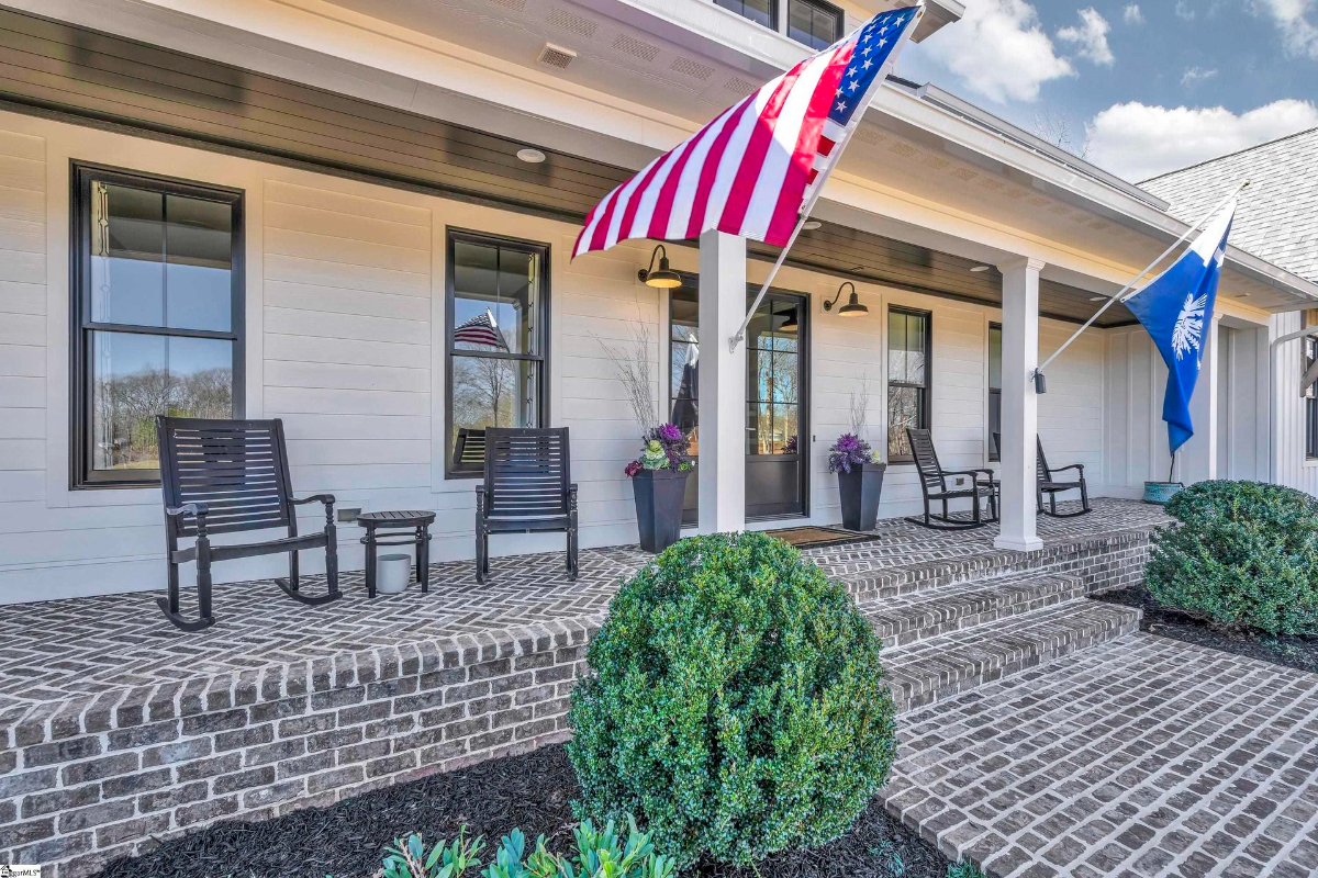 Welcoming front porch adorned with classic rocking chairs, vibrant potted plants, and patriotic flags.