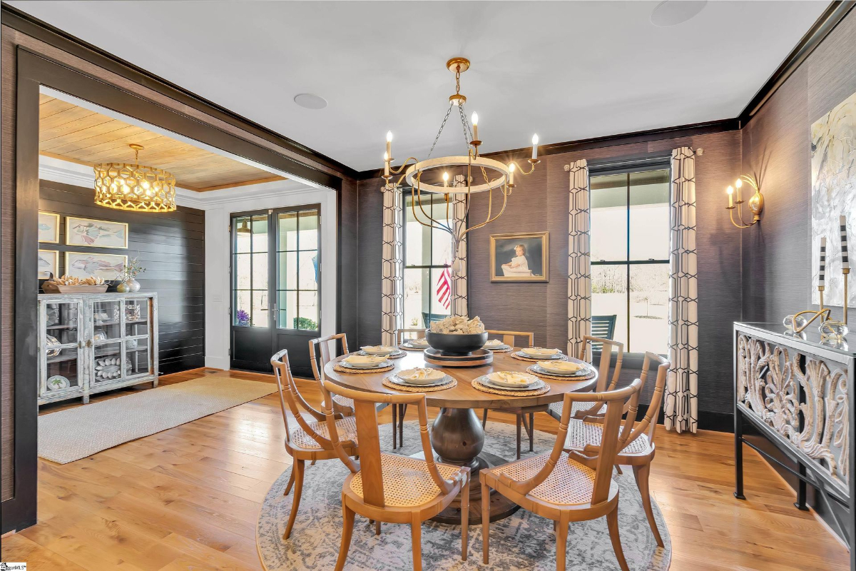 Elegant dining room with warm wood accents, a statement chandelier, and large windows framed by chic patterned curtains.