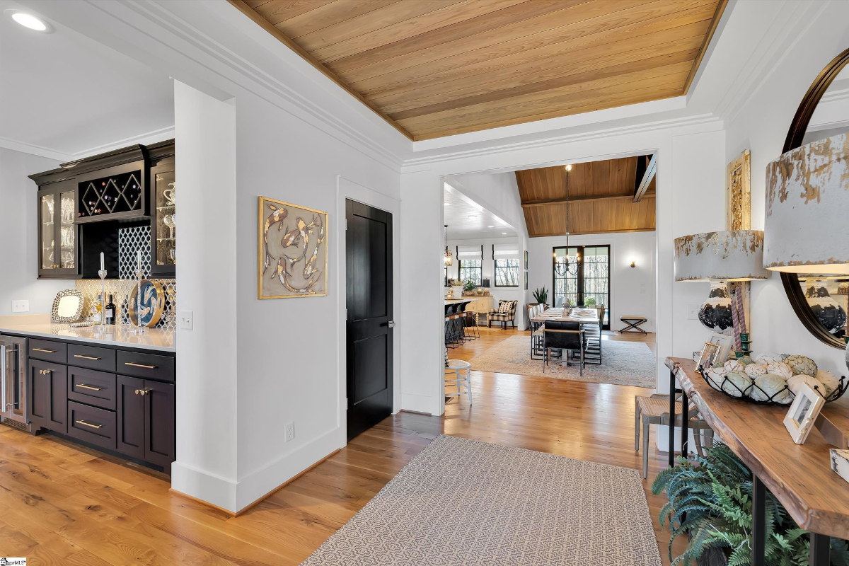 Stylish open-concept living space featuring a built-in bar, warm wood ceilings, and seamless flow into the dining and kitchen areas.