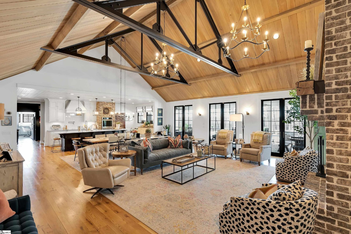 Spacious living area showcasing vaulted wood ceilings, exposed metal beams, elegant chandeliers, and a cozy open-plan design.