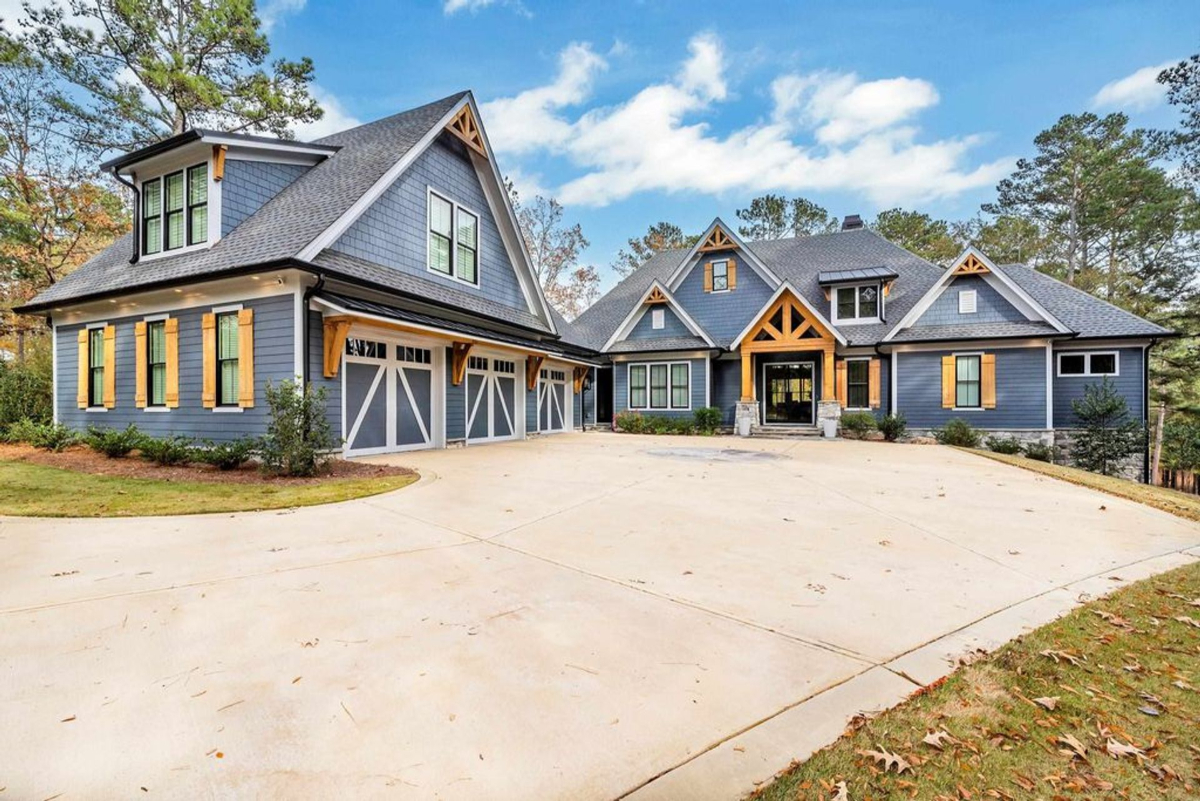 A charming Craftsman-style home showcases blue siding with natural wood accents, steep gabled roofs, and a spacious three-car garage.