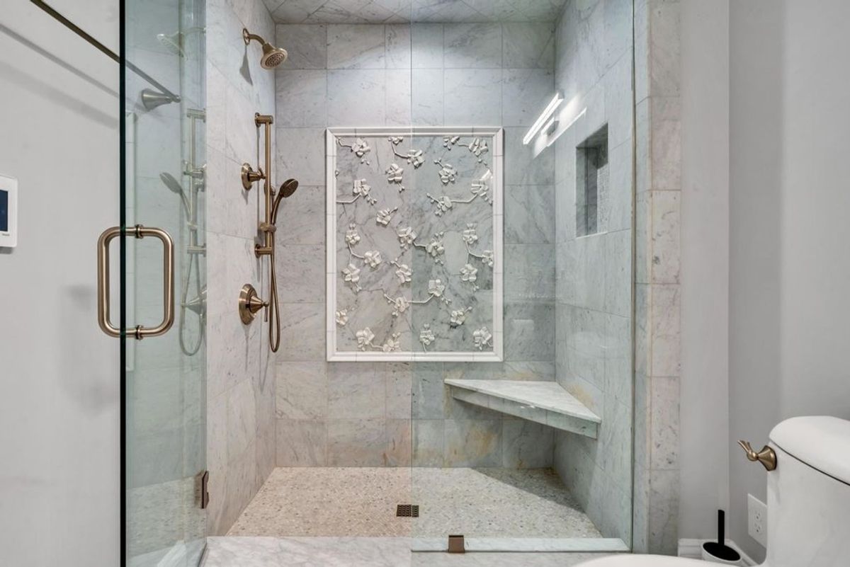 An elegant marble shower showcases a floral accent tile design, gold fixtures, and a corner bench for added luxury and comfort.