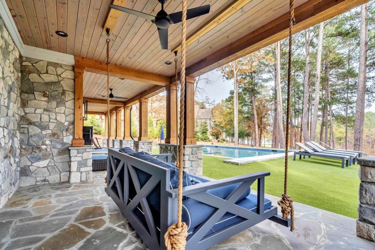 Outdoor retreat features a swing bed, stone accents, and a covered patio overlooking a sparkling pool surrounded by lush greenery.