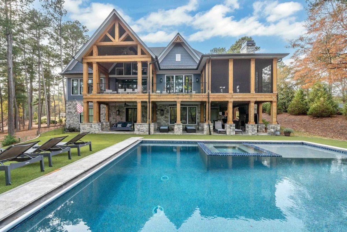 A magnificent two-story home showcases expansive wood and stone accents, screened porches, and a sparkling pool with a spa amidst lush surroundings.