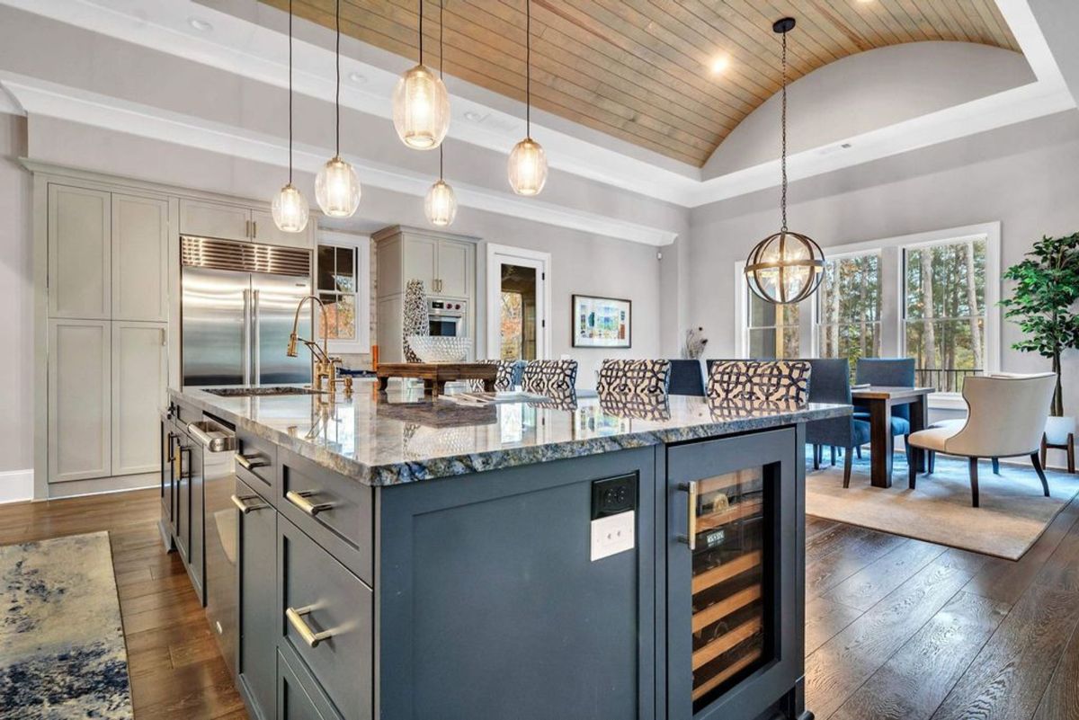 Kitchen island with a granite countertop and built-in wine cooler complements the arched wood ceiling and elegant lighting fixtures.