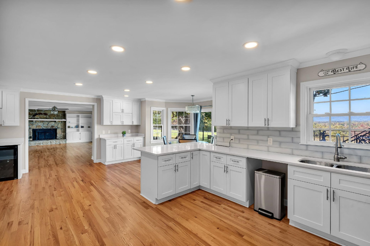 Kitchen features a large L-shaped counter, pristine white cabinetry, and a seamless flow into the adjacent family room with a stone fireplace.