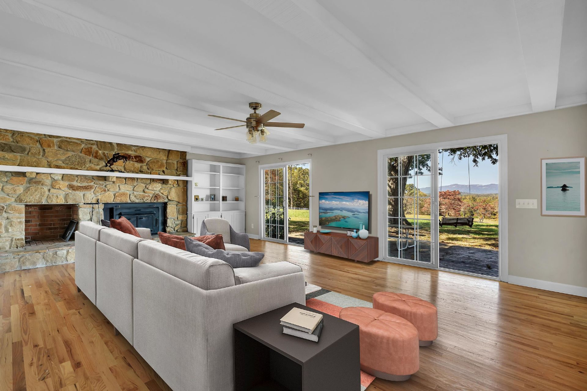 The cozy living room boasts a stone fireplace, exposed beam ceilings, and abundant natural light from sliding glass doors overlooking the scenic backyard.